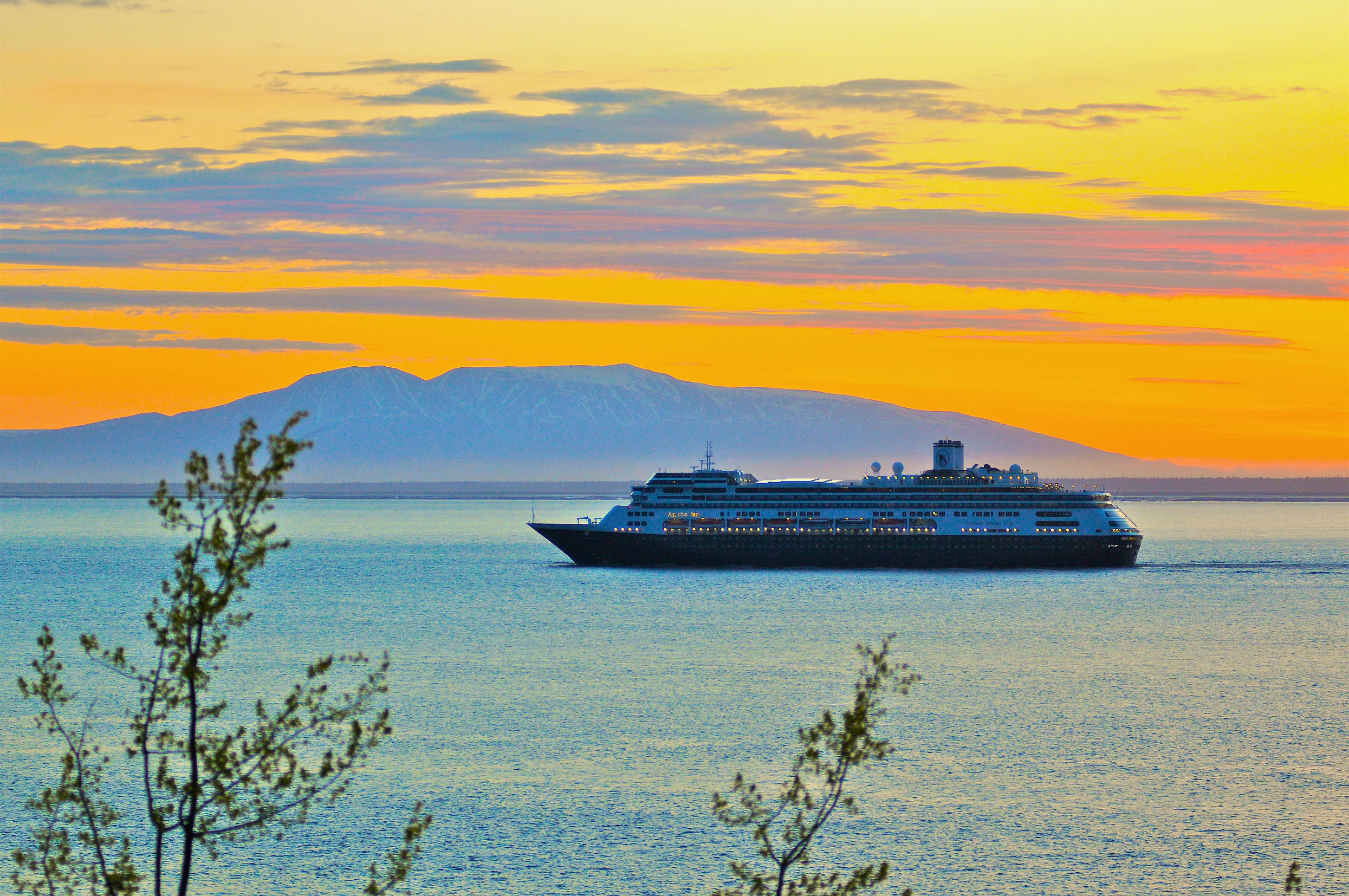 The best time to travel to Alaska: a cruise ship sailing by Alaska at sunset. 
