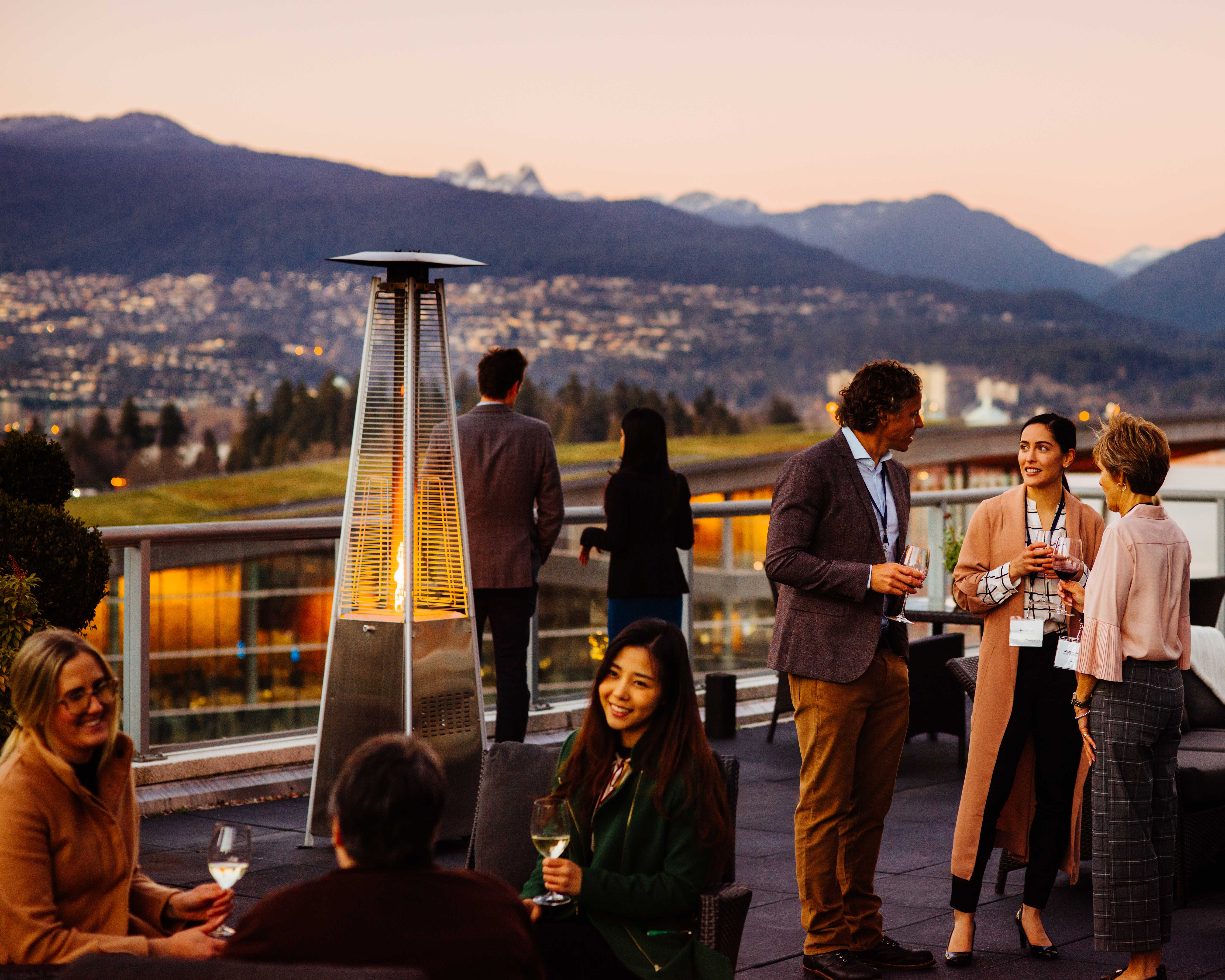 Vancouver vacations: people drinking on roof in Vancouver at sunset with the mountains in the background.