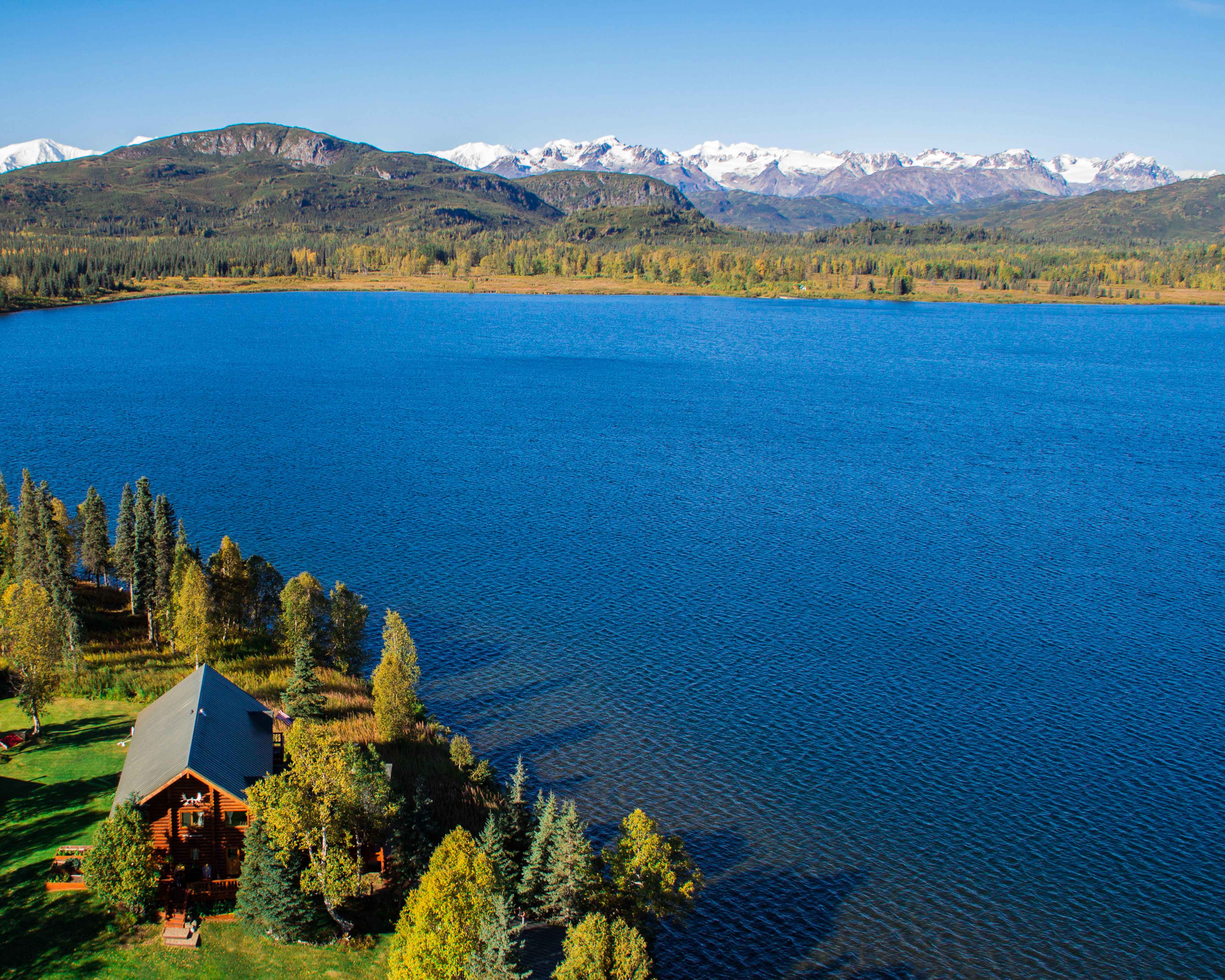 Finest lodges: lodge by the lake in Alaska with the mountains in the background.